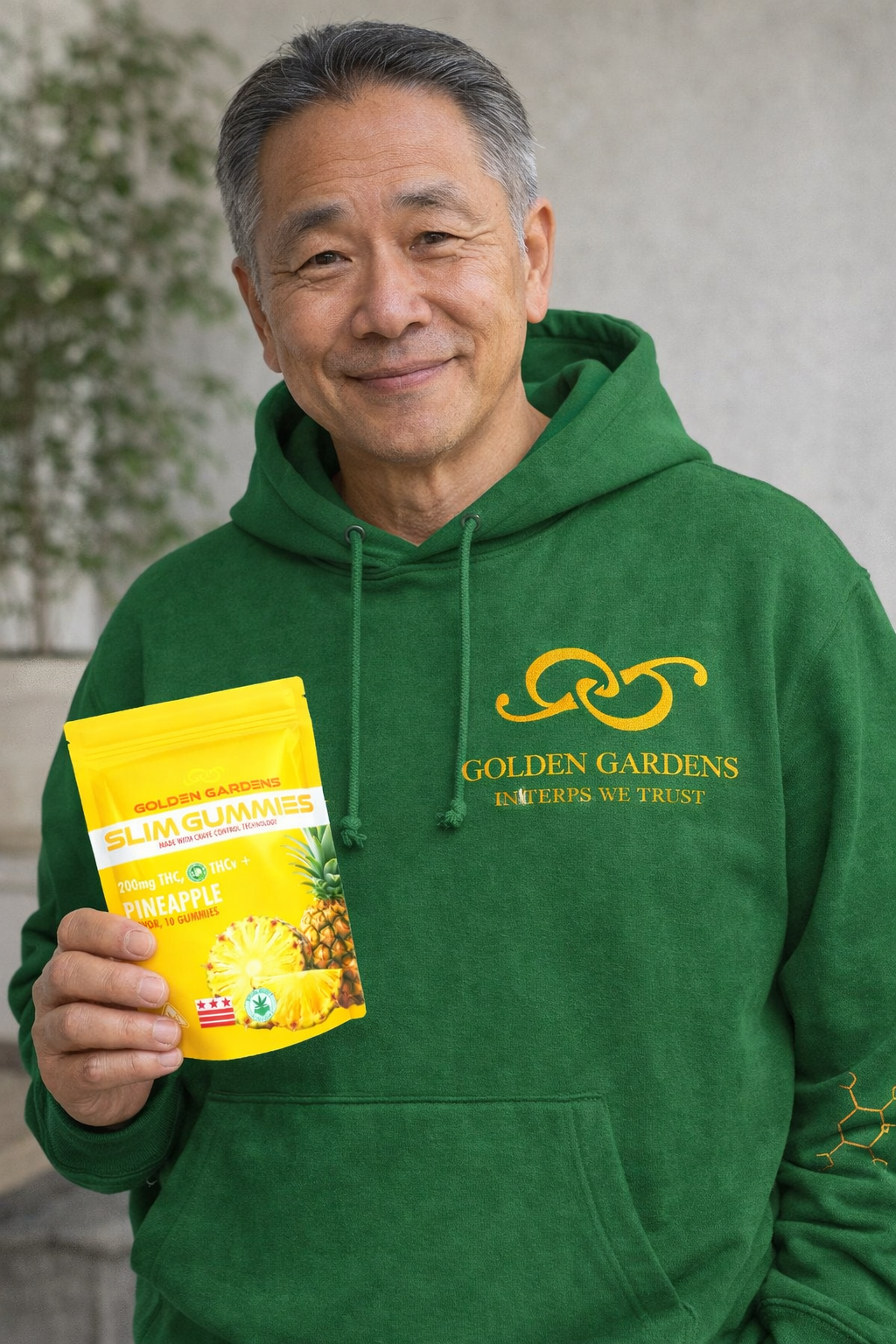 Man wearing a green 'Golden Gardens' hoodie holding Pineapple Slim Gummies